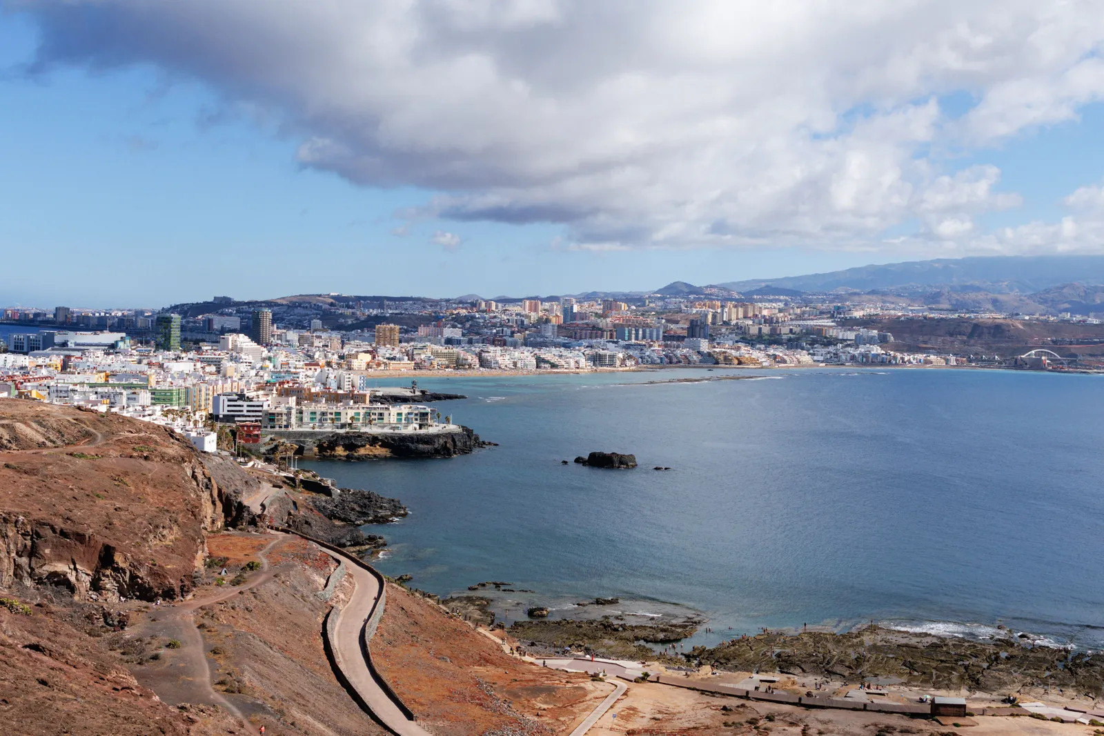A clifftop path above a bay, with a city across the water